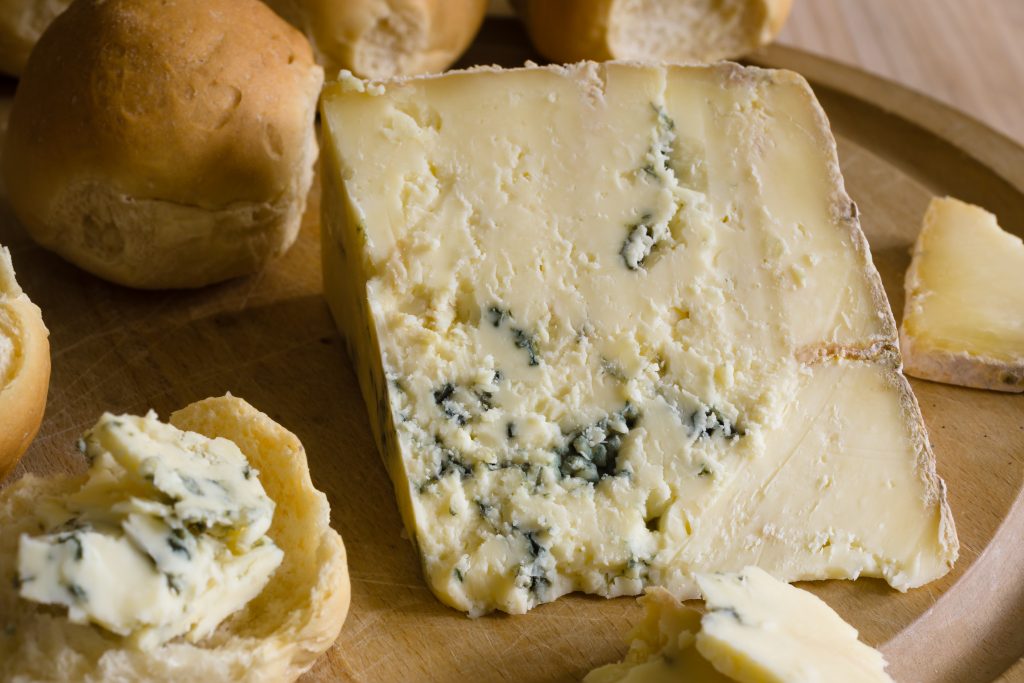Close up of a wedge of blue cheese surrounded by some small bread rolls on a wooden plate. Dorset Festivals Guide