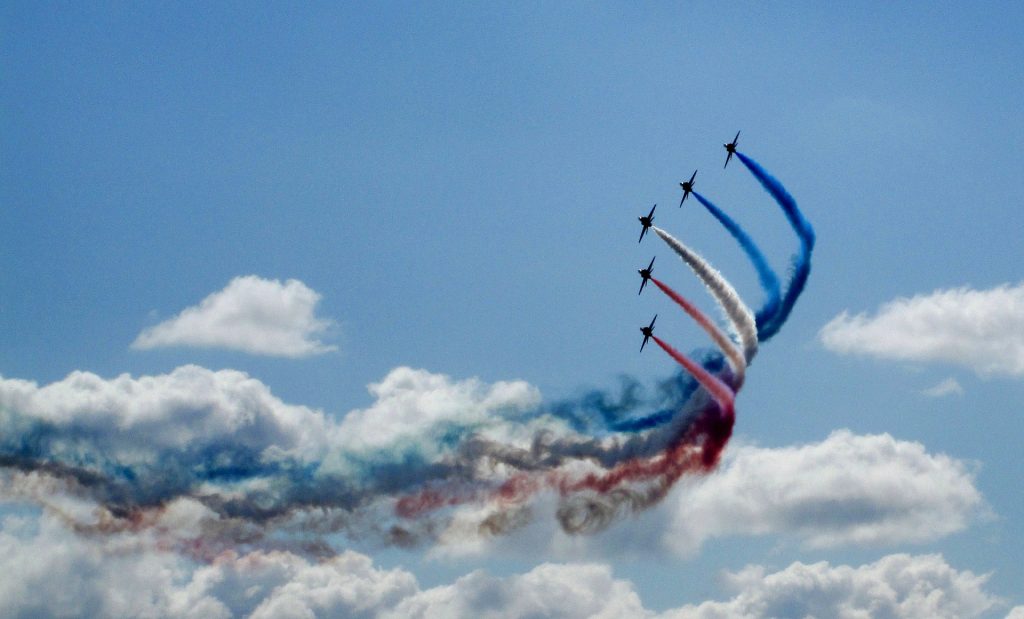 The Red Arrows airplanes flying in a triangle formation in the blue sky above a few white clouds with blue, red and white smoke trails behind them at Bournemouth Air Show. Dorset Festivals