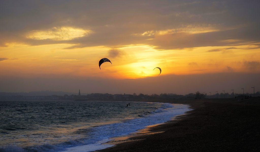 two kitesurfers with curved kites silhouetted against a golden sunset sky above the shingle on weymouth beach in dorset england