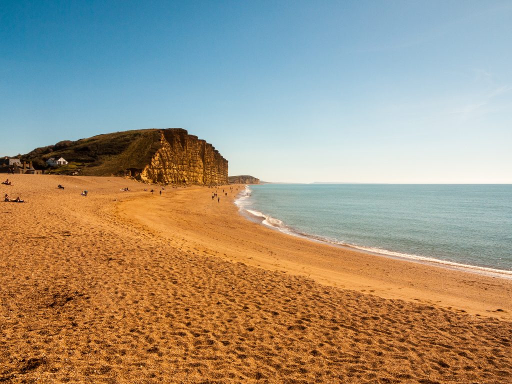 orange sand and shingle curved beach with very high orange cliffs in the background covered with grass, at West Bay near Bridport Dorset