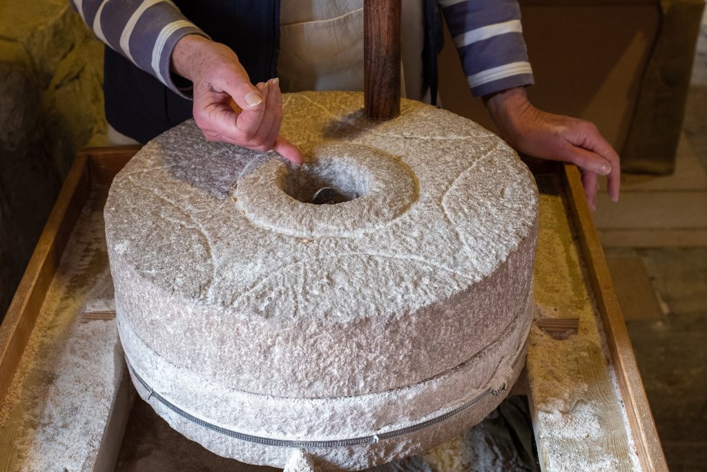 Close up of a large stone mill whieel with a star shape carved into it and a hand pointing at its centre - in Town Mill Lyme Regis