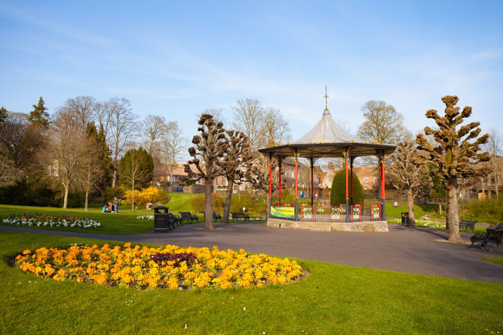 A bandstand with red pillars behind a circle of yellow flowers in Borough Gardens Dorchester - a perfect palce for a walk