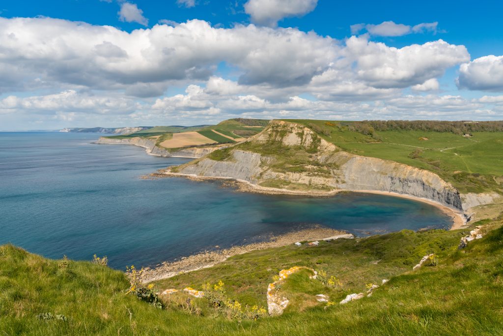 View from a grassy clifftop of Chapman's Pool, a small round cove with a narrow shingle beach and tall grey cliffs, near Worth Matravers on the Jurassic Coast