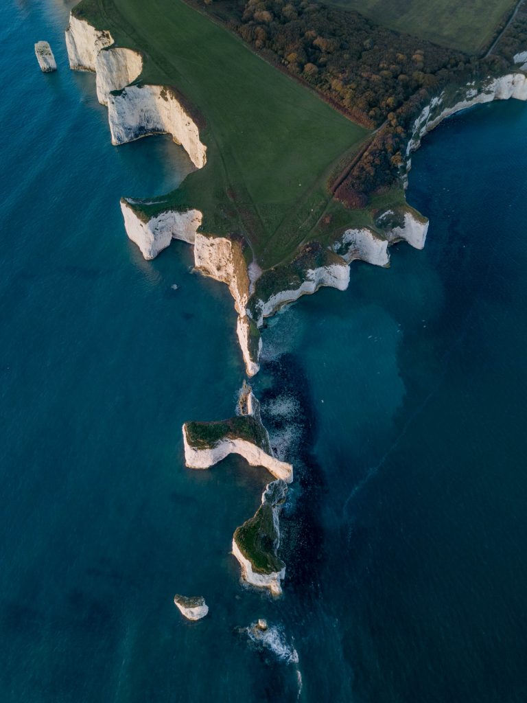 an aerial shot looking staight down at a grassy headland with a line of small rock stacks leading from it into the sea. Old Harry Rocks Dorset.