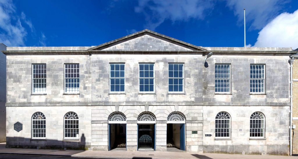 Exterior of the Shire Hall museum Dorcheste, a large grey stone manor with large windows and blue sky above. Things to do in Dorset in the rain