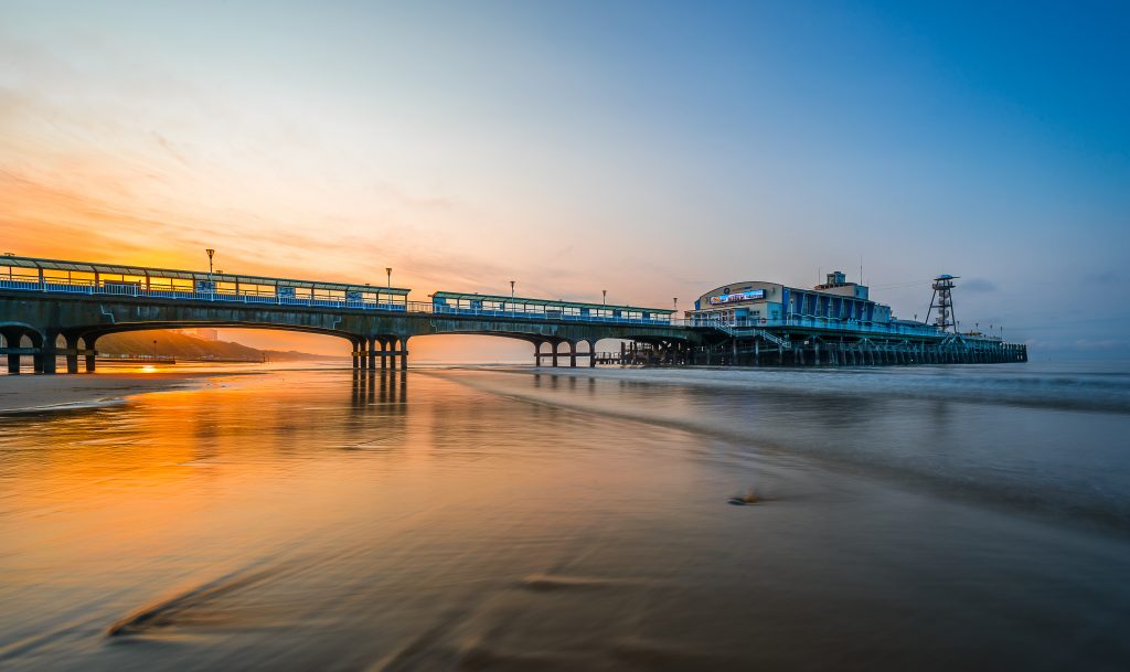 Shot of Bournemouth Pier at sunset with very calm sea at low tide reflecting the orange of the sunset and the pier silhouetted against the sky