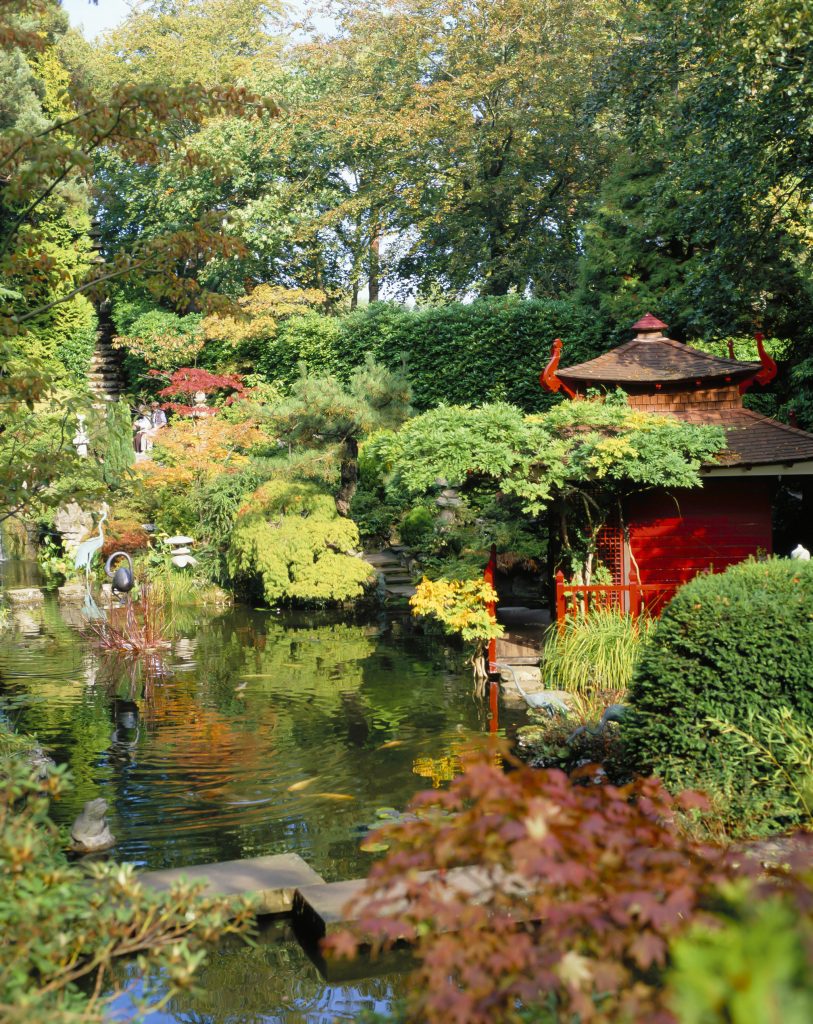 small pond with still watyer surrounded by greenery and trees with a stone japanese style sculpture at Compton Acres gardens in Poole Dorset