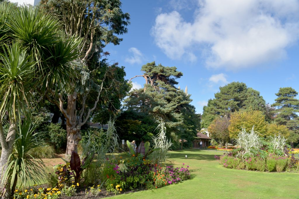 Landscape in the Lower gardens in Bournemouth town centre with many hedges and green leafy trees around a neat lawn with a few flower beds 