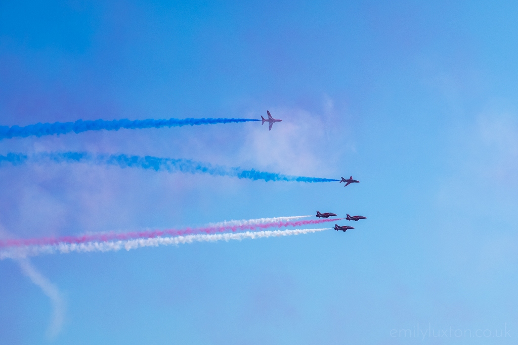 Red Arrows airplanes flying through the blue sky with trails of red and blue coloured smoke behind them at an Air Festival