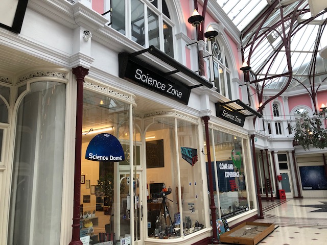 Exterior of Scienze Zone, a kids Activity Centre in Bournemouth, the centre is in a white painted shop with a glass storefront inside a small shopping mall with pink painted walls and a glass roof