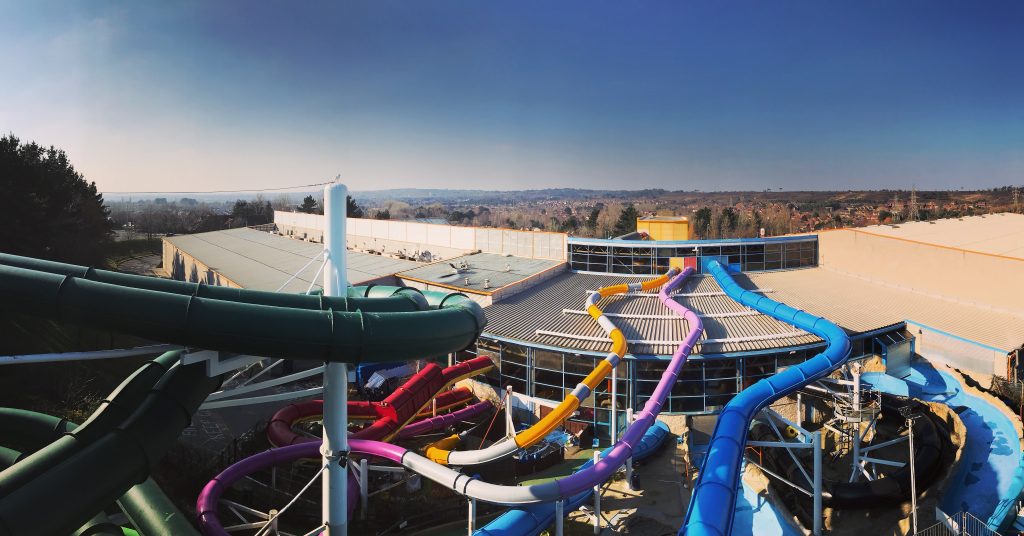 exterior of a large indoor water park with a grey roof and several long flumes in different colours around the outside of the building. Things to do in Dorset in the rain.