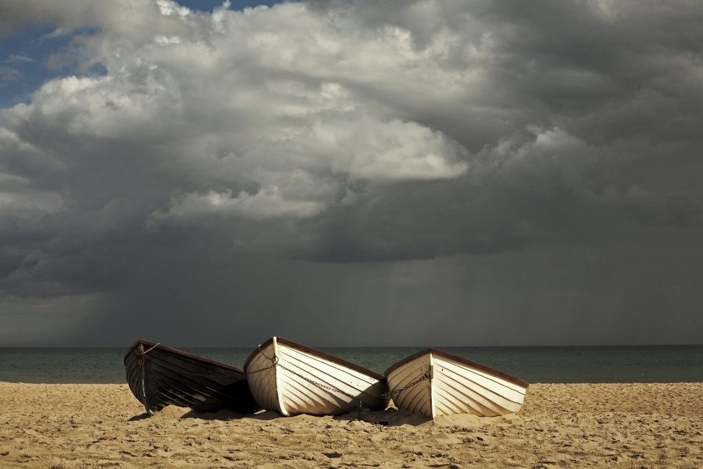 a three small white wooden rowing boats on a beach with dark clouds overhead - things to do in dorset in the rain