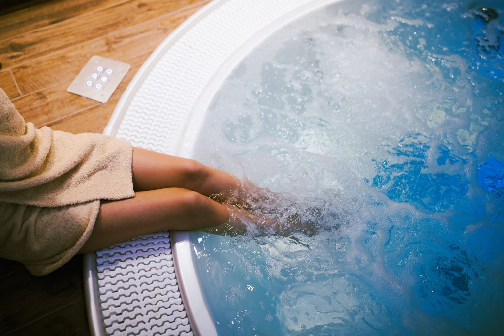 a woman's legs dangling into a bubbling hot tub viewed from above - Spas in Dorset for a rainy day