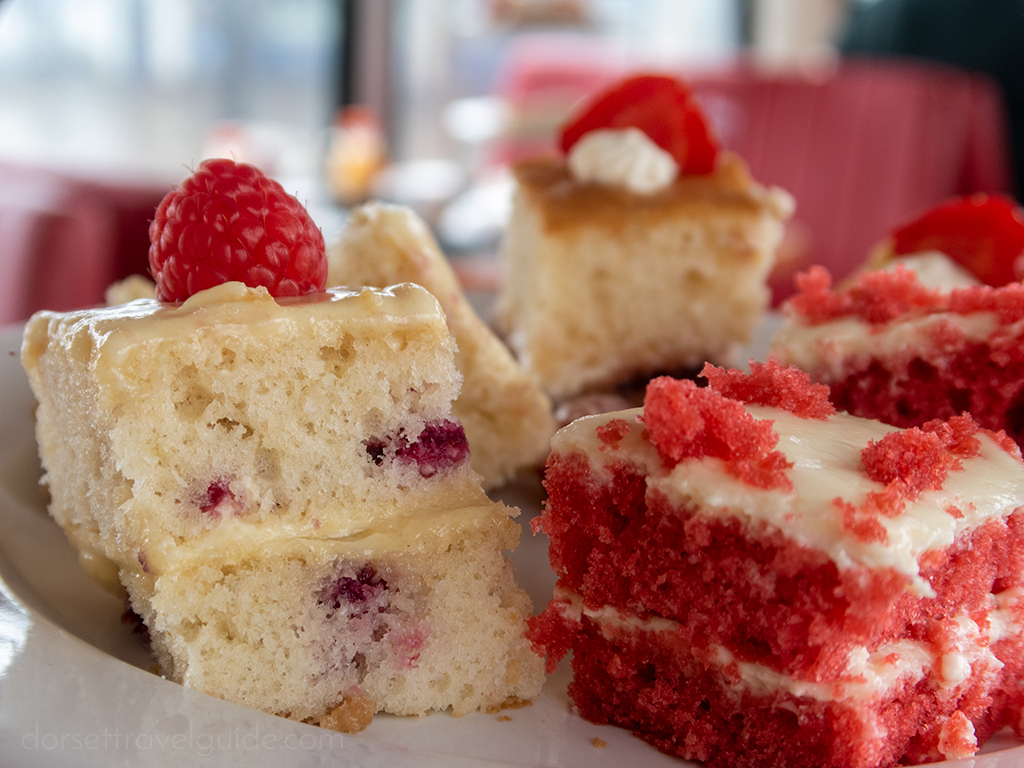 three small sponge cakes, two white and one red, with cream filling and cream frosting topped with raspberries on a white plate