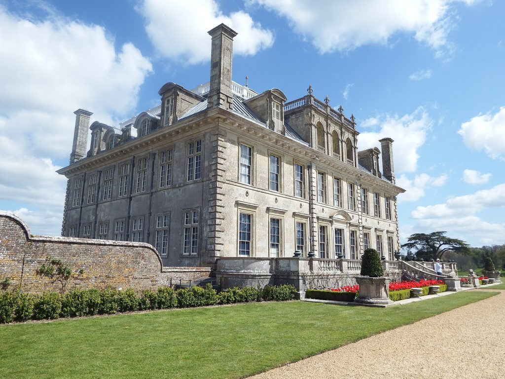 exterior of a large white stately home with a lawn in front on a sunny day with blue sky with some small fluffy clouds. Kingston Lacy Dorset Stately Homes