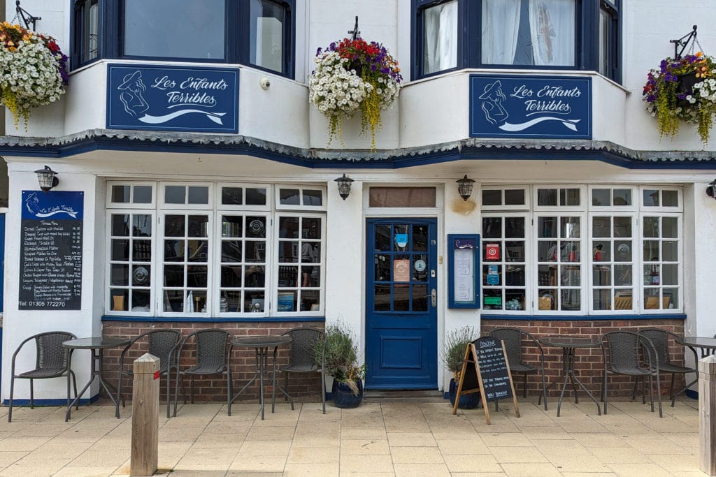 exterior of Les Enfants Terribles restaurant in weymouth in a whitewashed building with dark blue trim and a blue door