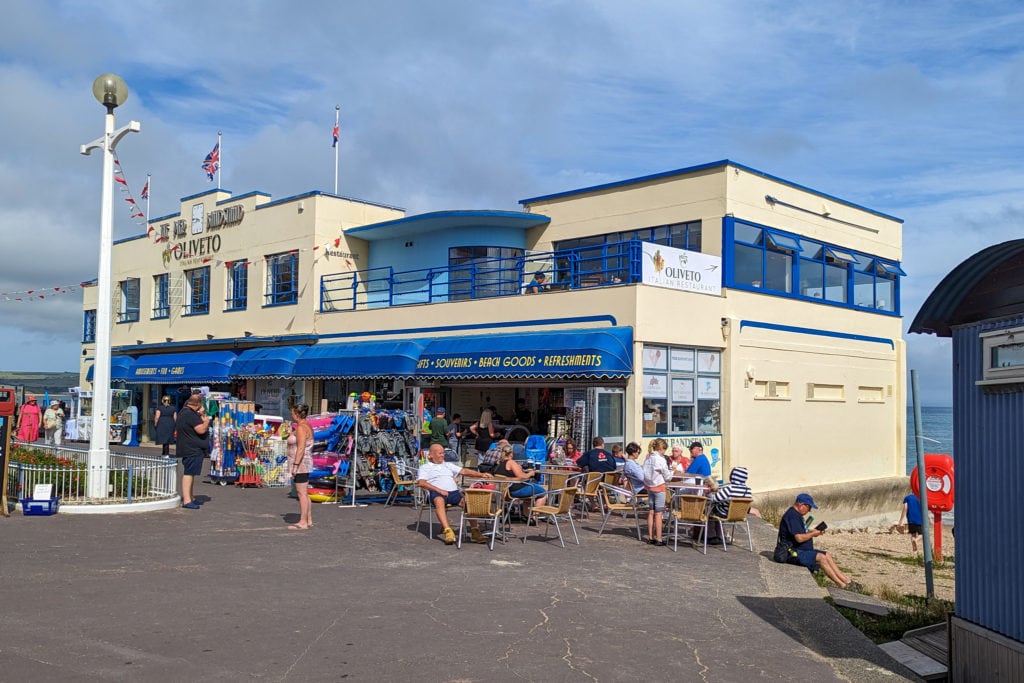 yellow and blue two-storey bandstand on Weymouth esplanade with blue awning above an amusement arcade and a small ice cream shop