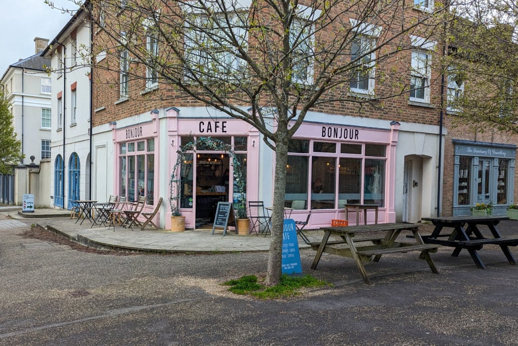 exterior of a cafe with pink painted walls and the name Bonjour Cafe printed in black over the door on a quier pedestrian street with a bare tree outside