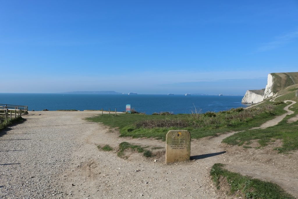 gravel path on a grassy cliff top with a view of the sea and some white chalk cliffs 