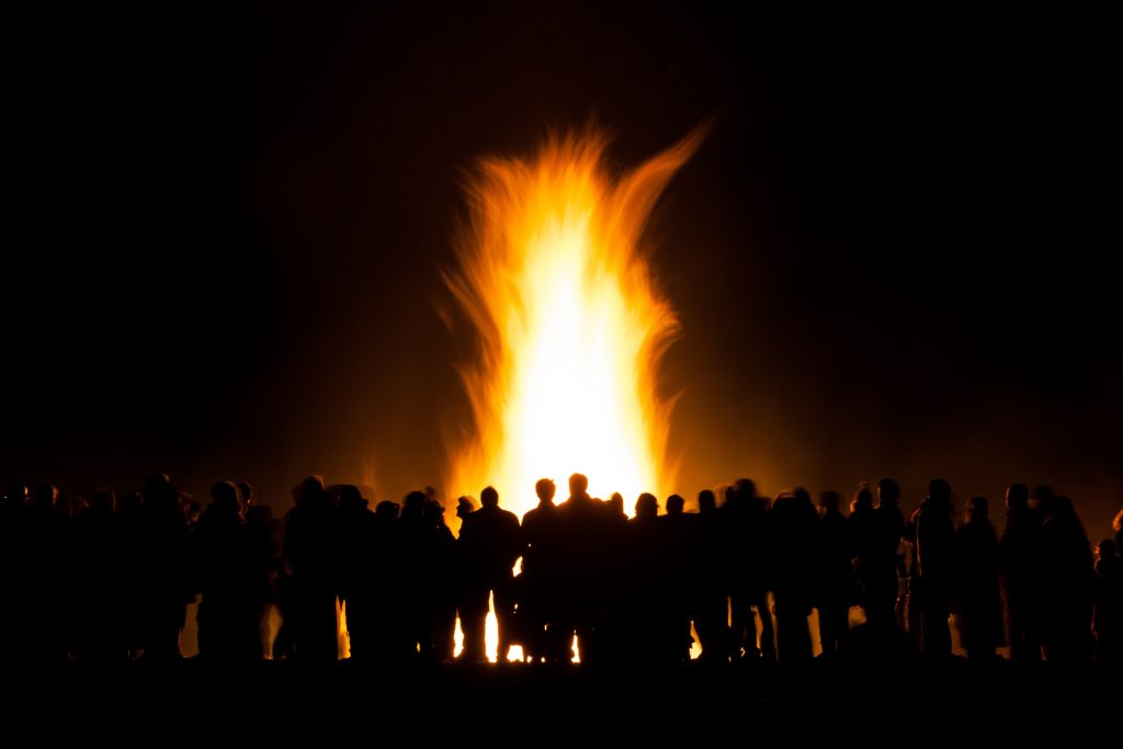 Crowd of people silhouetted in front of a large bonfire against the night sky. 