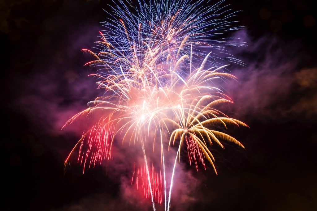 Fireworks exploding in the night sky creating a cluster of star shapes in orange, blue and red.