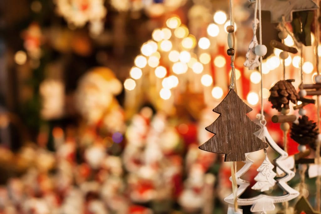Wooden christmas tree shaped decorations hanging from a market stall with fairy lights out of focus behind. Bournemouth Christmas Markets