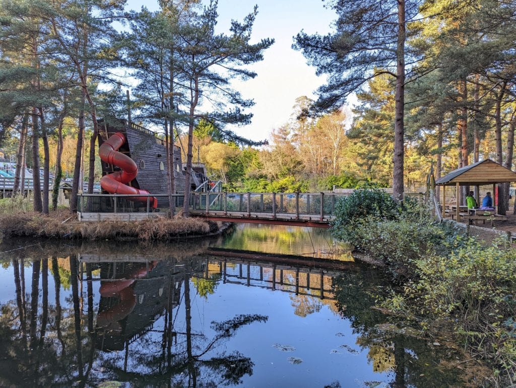a still pond surrounded by pine trees with a wooden pirate ship 