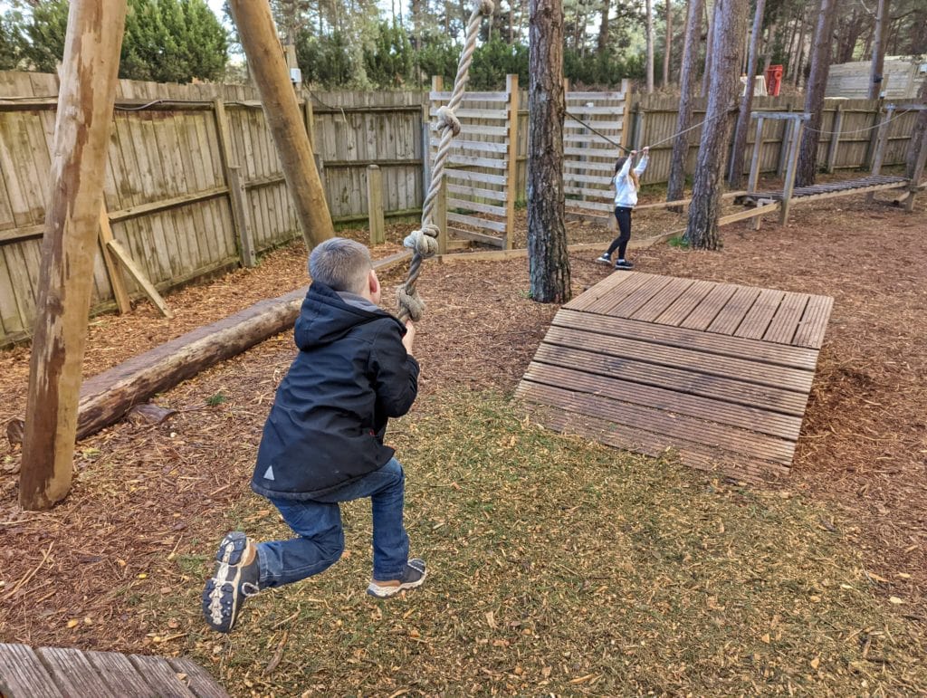 a small boy riding a rope swing between two wooden platforms at Snowtrax in Bournemouth