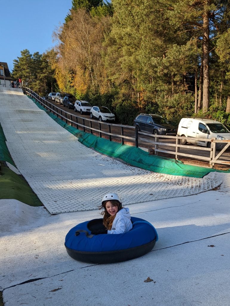 A small girl in a white hoody riding a blue tyre down the Ringos slope 