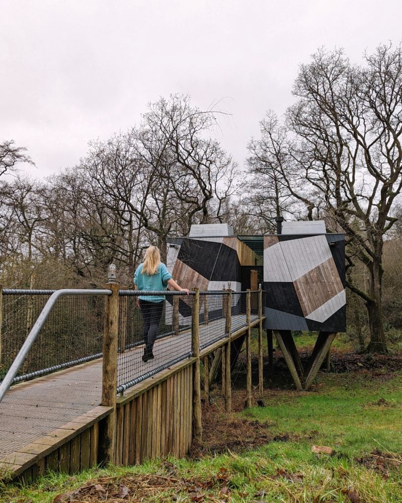 girl with blonde hair and turquoise jumpred crossing a wooden bridge towards a treehouse in dorset