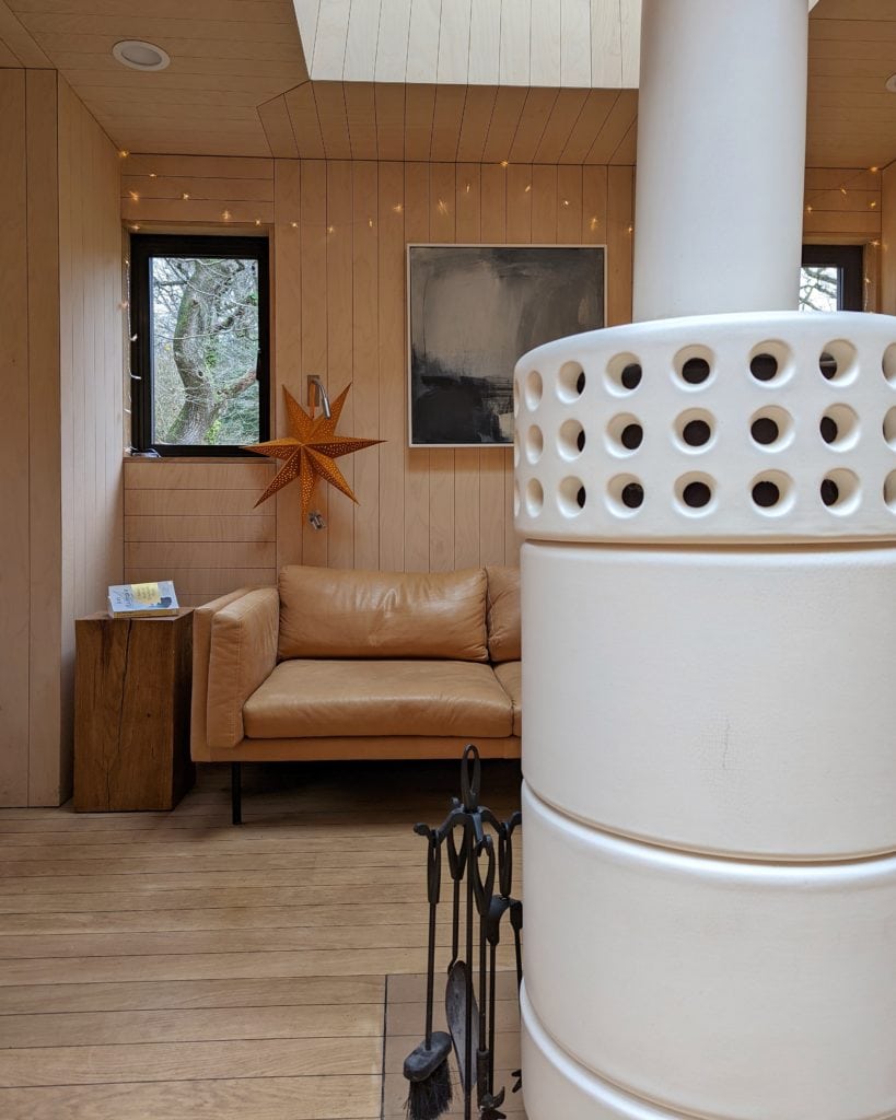 white log burner with a leather sofa behind it inside a wooden treehouse in dorset