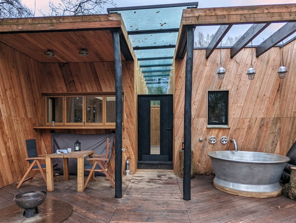 wooden deck area behind a log cabin with wooden furniture, a firepit, and a metal hot tub