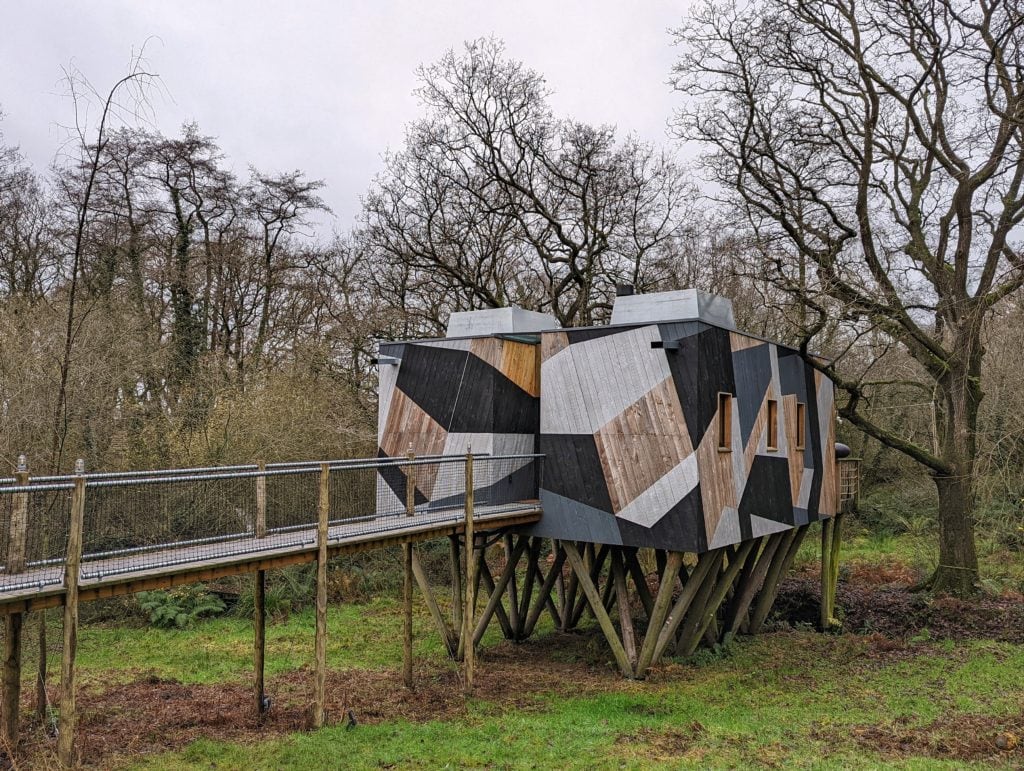 Dazzle treehouse, a small log cabin painted in grey and wooden stripes betwen bare trees in winter in West Dorset