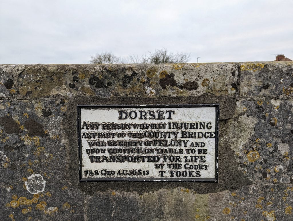 an old plaque on a stone wall which reads: "Dorset Any person wilfully ingjuring any part of this county bridge will be guilty of felony and upon conviction liable to be transported for life by the court"