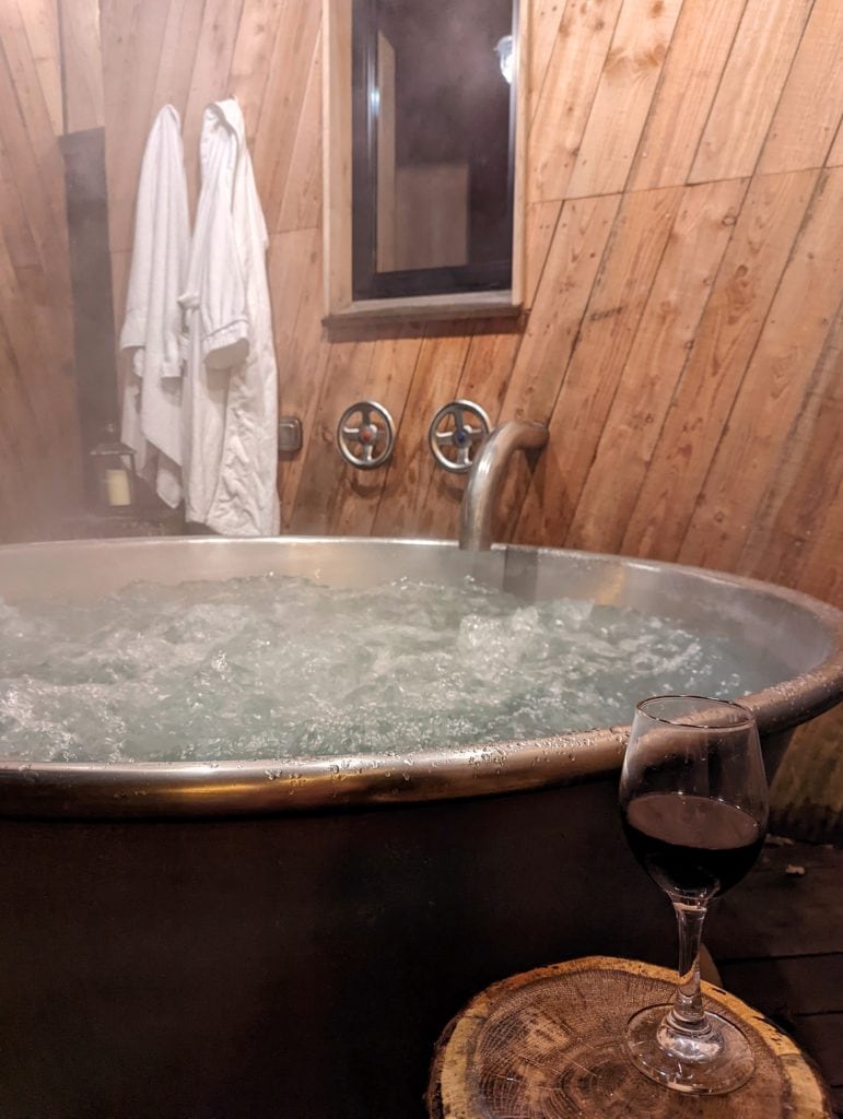hot tub filled with bubbling water with a white dressing gown hanging up behind it and a glass of wine in the foreground