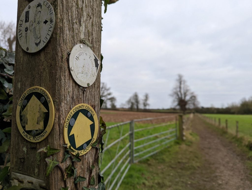 wooden signpost near dorchester with walk route markers on it and a muddy path in the background