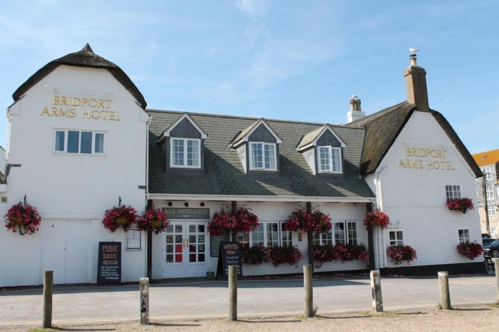 a pub hotel on the dorset coast with white washed exterior and grey slate roof in front of a blue sky