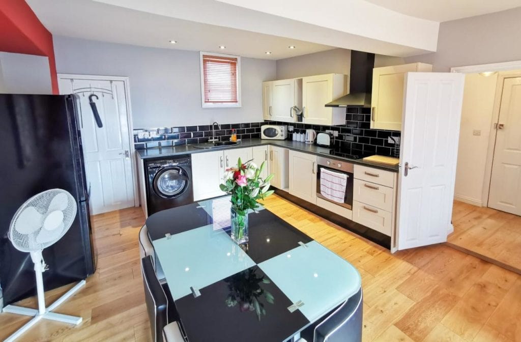 a modern kitchen with a wooden floor, white cupboards, black tiles, and a glass table