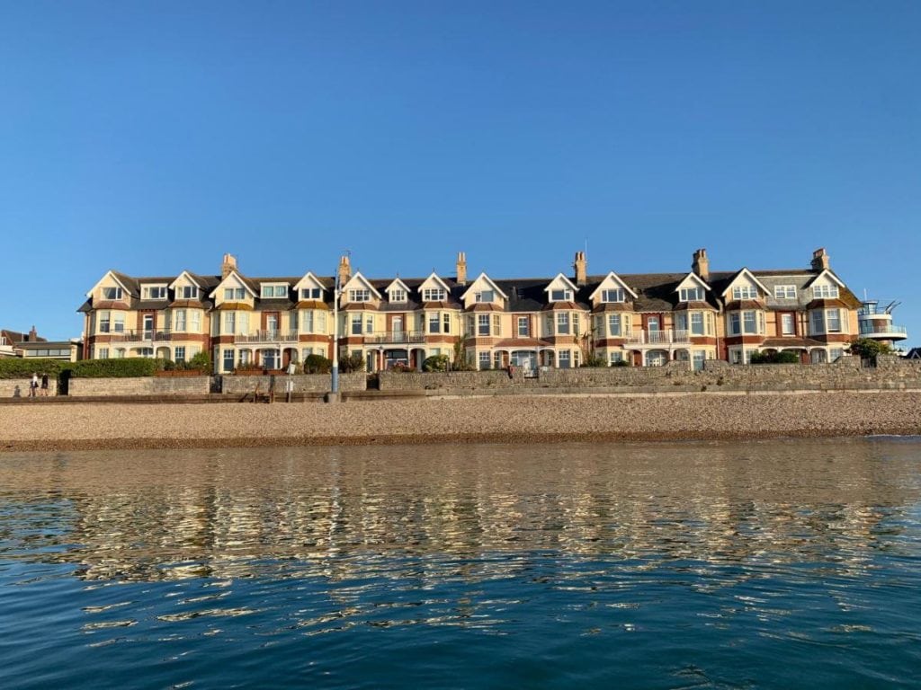 taken from the sea with water in the foreground and a row of terraced holiday homes in weymouth against a blue sky