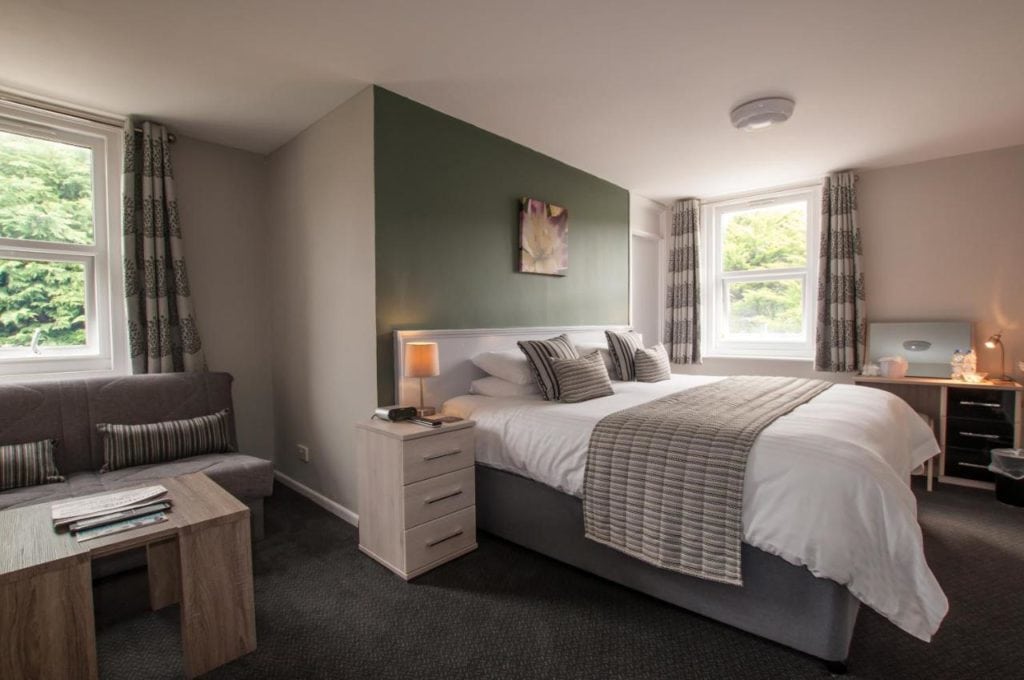 neatly made hotel bed with white sheets and a grey throw in front of a grey wall