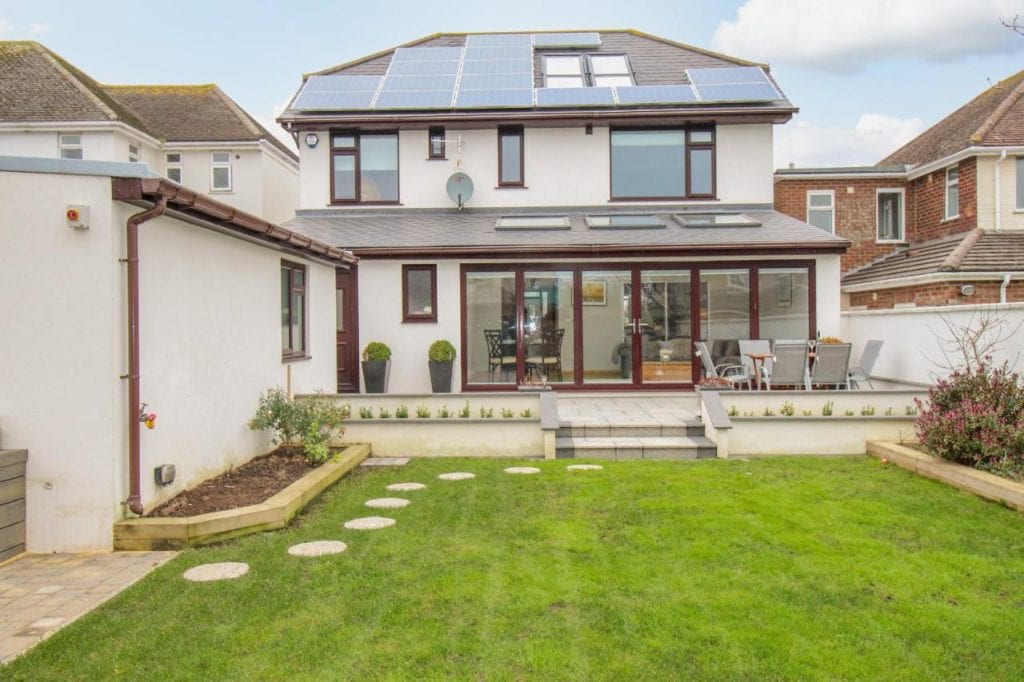 exterior of a large cream house big windows and solar panels on the slate tiled roof. 