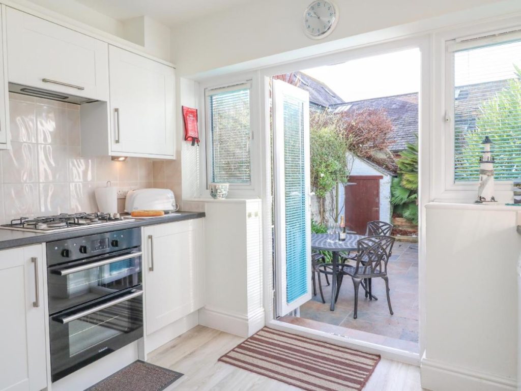 a white kitchen with the back door open to reveal a small garden with a bottle or wine and glasses on a table  - best holiday homes in weymouth