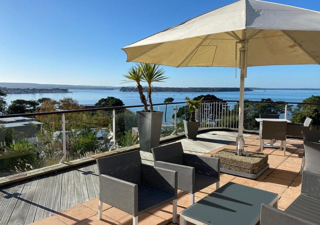 table and chairs on a verandah with a white umbrella with the sea behind - coastal hotels in dorset