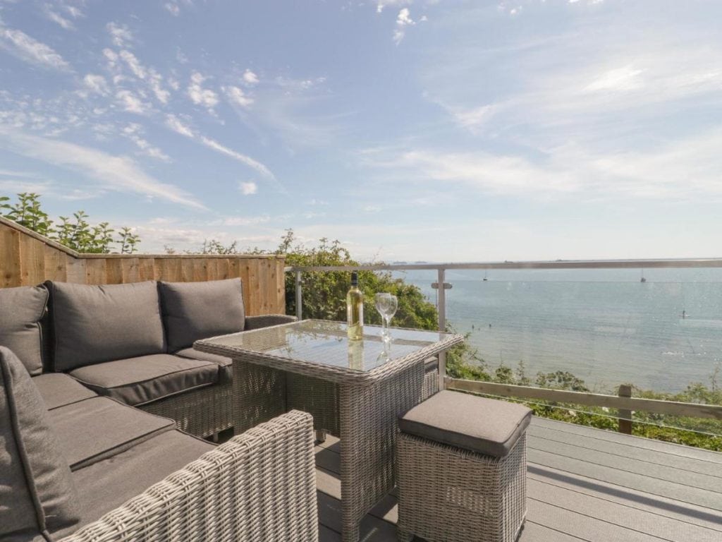 grey garden furniture on a balcony overlooking the sea with a bottle of wine and glasses on the table 