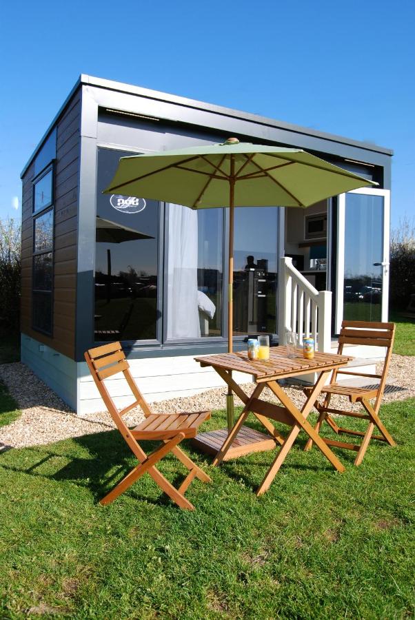 wooden table and chairs on the grass in front of a square holiday lodge covered in grey plastic cladding with french doors open on a sunny day in weymouth