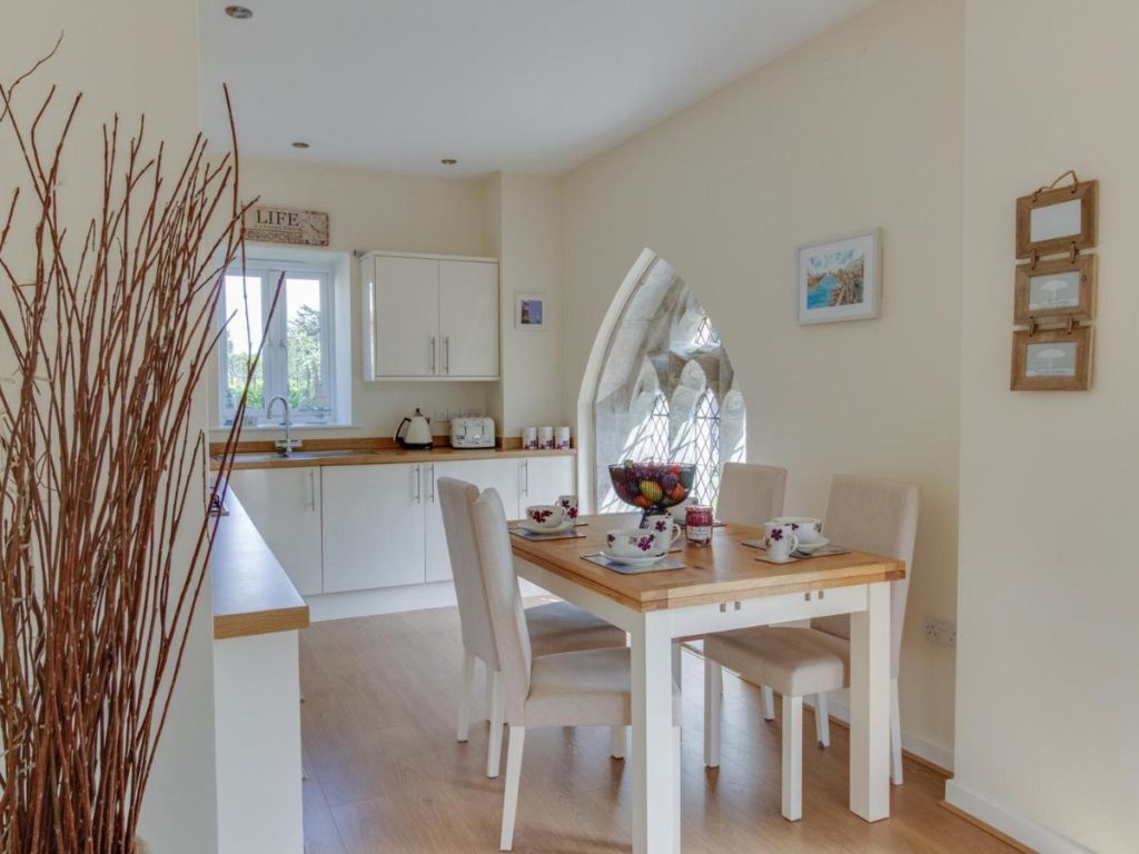 a white kitchen with white cupboards and wooden worktops with a wooden dining table