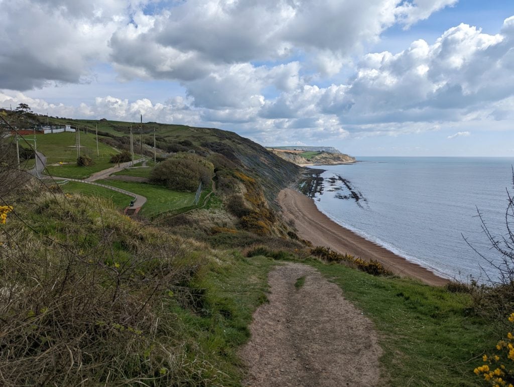 looking down from a low cliff towards a shingle beach. there are a few wooden structures on the cliffs overlooking the beach in a holiday park.