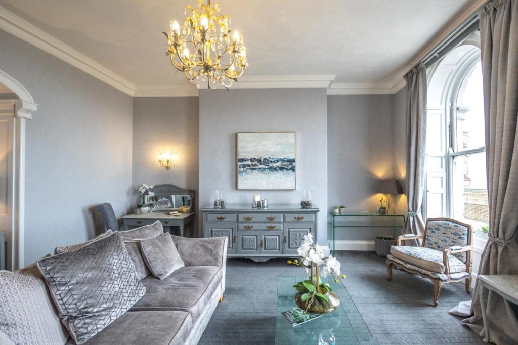 a hotel room painted light grey with a grey sofa and wooden furniture painted blue grey 