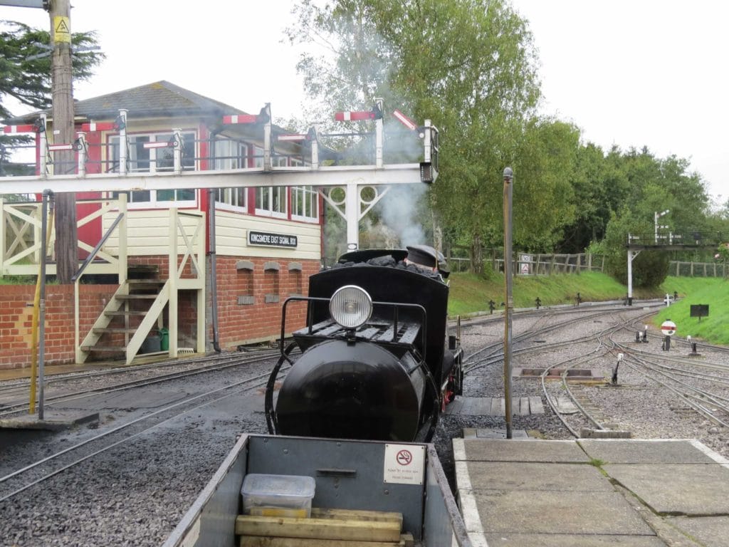 a small black narrow guage steam engine on a track next to a small ed brick bulding with cream cladding and a sign which reads kingsmere east signal box. Moors Valley country park is one of the best things to do near bournemouth with kids.