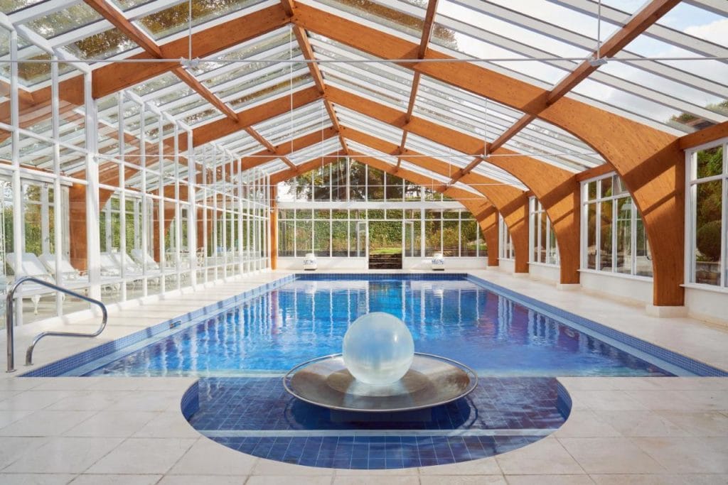 a large glass conservatory with a rectangular swimming pool. there is a glass ball in front of the pool on a blue tiled semicircle. best hotels with spas in dorset. 